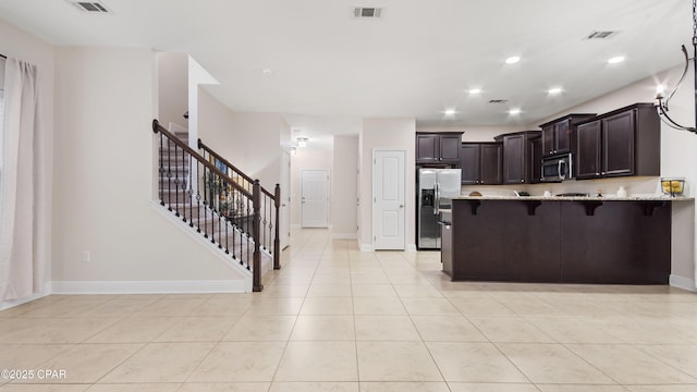 76 Mosaic Oaks Cir, Santa Rosa Beach, FL 32459 - kitchen featuring appliances with stainless steel finishes, a kitchen bar, dark brown cabinetry, light stone countertops, and a peninsula