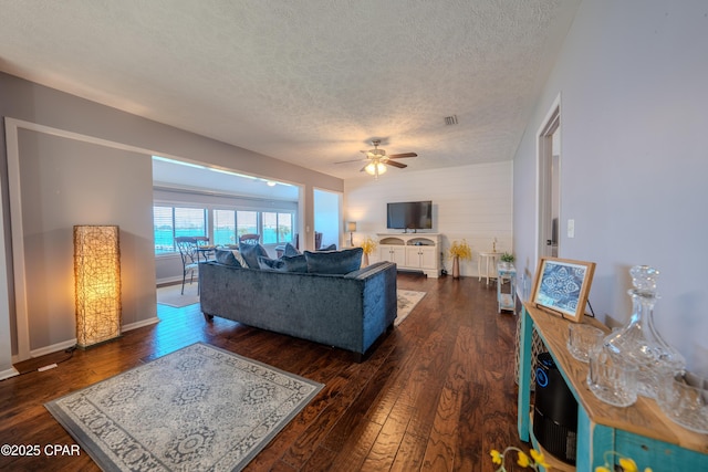 living area featuring a textured ceiling, ceiling fan, dark wood-style flooring, and baseboards