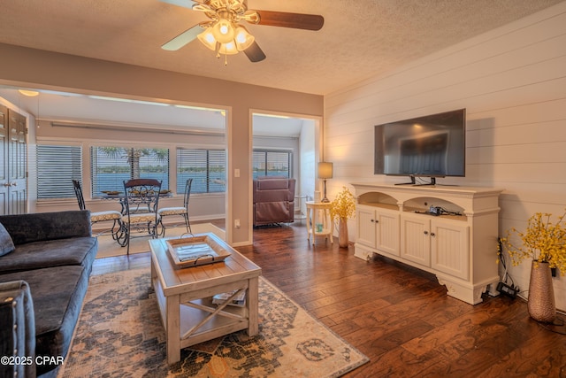 living room with dark wood-type flooring, ceiling fan, a textured ceiling, wood walls, and baseboards