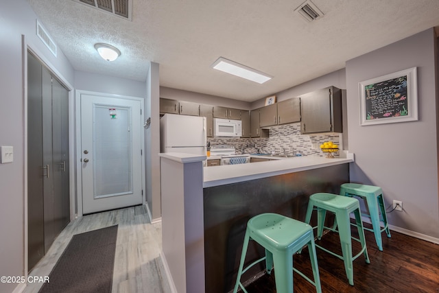 kitchen with white appliances, light wood-type flooring, a peninsula, a textured ceiling, and backsplash