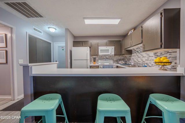 kitchen featuring white appliances, backsplash, a peninsula, light countertops, and wood finished floors