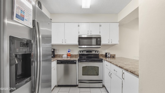 kitchen with stainless steel appliances, white cabinets, light tile patterned floors, and a textured ceiling