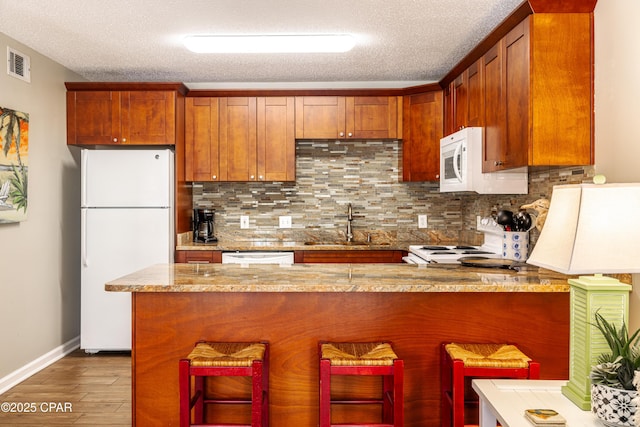 kitchen featuring white appliances, a sink, decorative backsplash, wood finished floors, and a textured ceiling