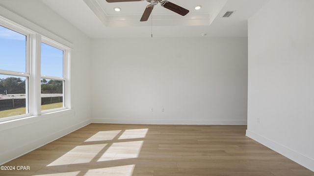 empty room with a raised ceiling, plenty of natural light, light wood-style floors, baseboards, and recessed lighting