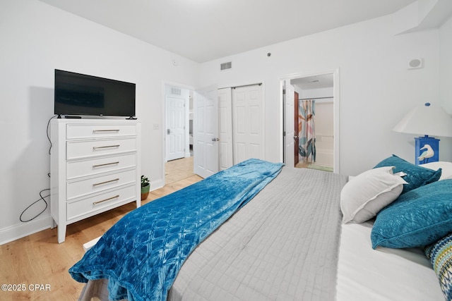 bedroom with light wood-type flooring, baseboards, a closet, and ensuite bath