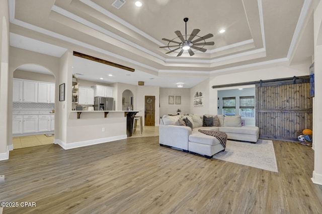 1104 Zephyr, Panama City, FL 32404 - living room featuring a tray ceiling, arched walkways, a ceiling fan, light wood-style flooring, and a barn door