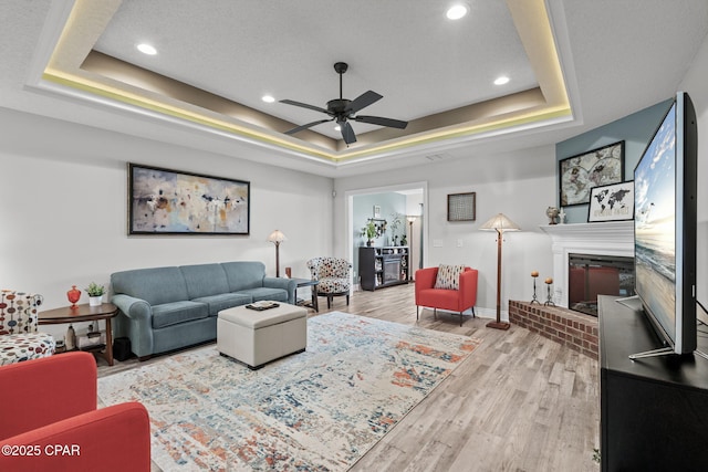 4724 Bylsma Cir, Panama City, FL 32404 - living area featuring a tray ceiling, a fireplace, a ceiling fan, baseboards, and wood finished floors