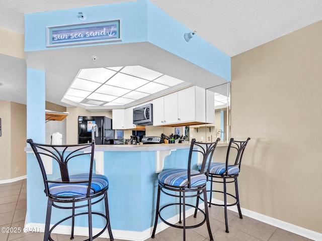 6505 Thomas Dr Unit 1009B, Panama City Beach, FL 32408 - kitchen featuring freestanding refrigerator, stainless steel microwave, light tile patterned flooring, a peninsula, and white cabinetry