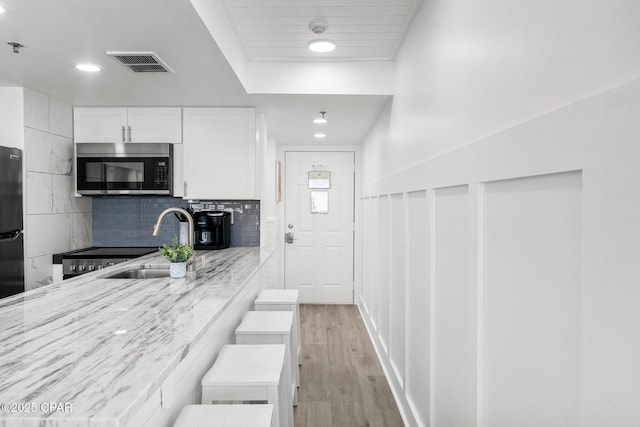 9850 S Thomas Dr Unit 1112E, Panama City Beach, FL 32408 - kitchen featuring stainless steel microwave, a sink, light wood finished floors, white cabinets, and freestanding refrigerator