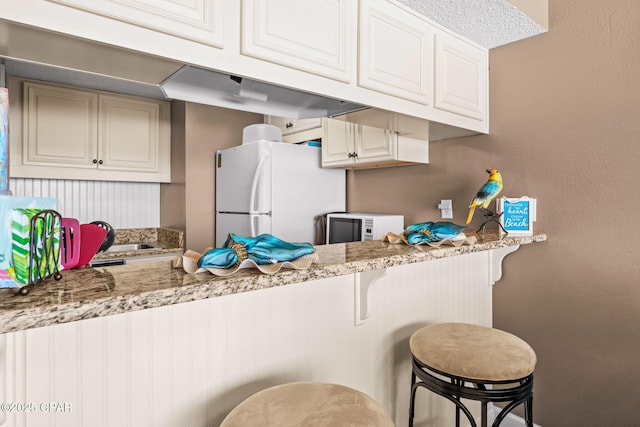 23223 Front Beach Rd Unit A509, Panama City Beach, FL 32413 - kitchen with white appliances, light stone countertops, a peninsula, and a kitchen bar