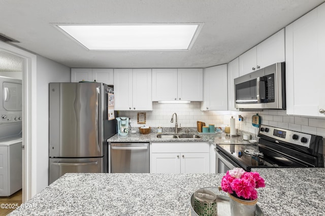 23223 Front Beach Rd Unit A704, Panama City Beach, FL 32413 - kitchen featuring appliances with stainless steel finishes, a sink, estacked washer and dryer, white cabinets, and decorative backsplash