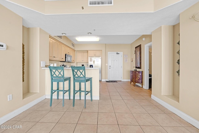 8715 Surf Dr Unit 304B, Panama City, FL 32408 - kitchen featuring stainless steel appliances, light brown cabinetry, a peninsula, light tile patterned floors, and a kitchen breakfast bar