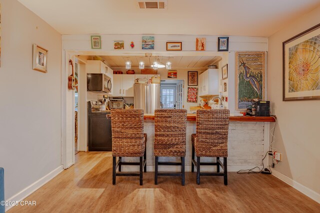 5821 S Lagoon Dr, Panama City, FL 32408 - kitchen with appliances with stainless steel finishes, light wood-style floors, a peninsula, a kitchen bar, and baseboards