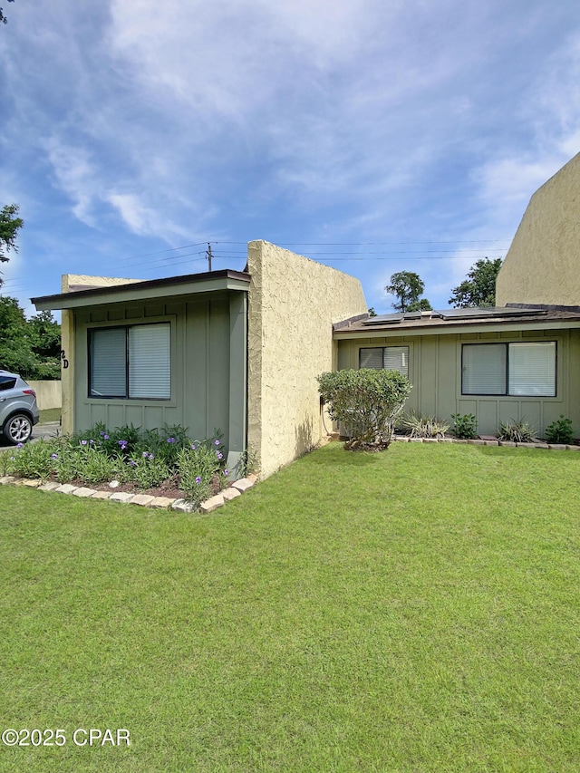 1025 W 19th St Unit 2D, Panama City, FL 32405 - view of property exterior featuring board and batten siding, solar panels, and a yard