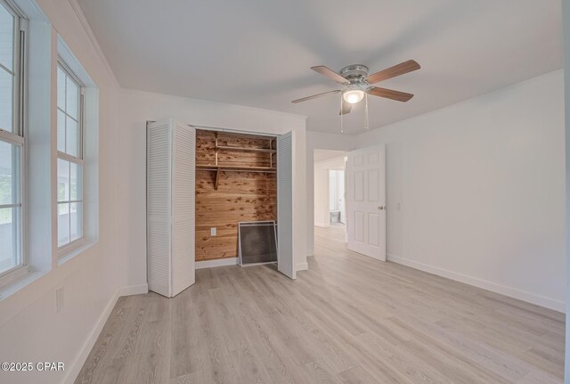 25966 George Maloy Ln, Altha, FL 32421 - unfurnished bedroom featuring light wood-style flooring, baseboards, wooden walls, a closet, and a ceiling fan