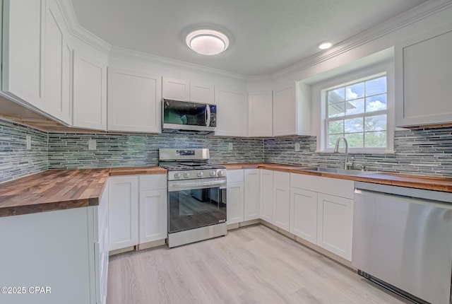 25966 George Maloy Ln, Altha, FL 32421 - kitchen featuring butcher block countertops, appliances with stainless steel finishes, a sink, white cabinetry, and decorative backsplash