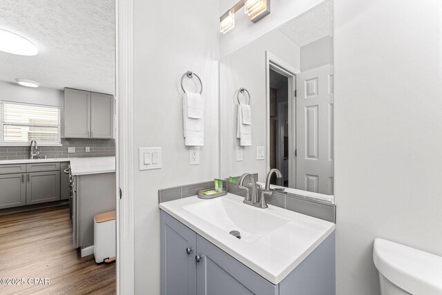 190 White Cap Way, Panama City Beach, FL 32407 - bathroom featuring a textured ceiling, vanity, backsplash, wood finished floors, and toilet
