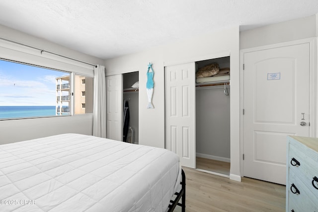 23223 Front Beach Rd Unit C1-502, Panama City Beach, FL 32413 - bedroom with two closets, light wood finished floors, a textured ceiling, a water view, and baseboards
