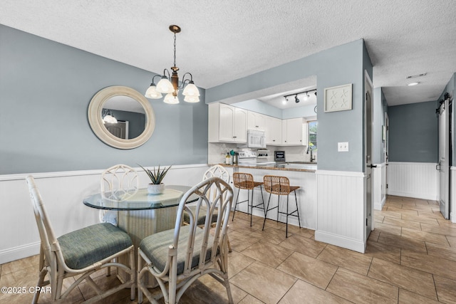 17620 Front Beach Rd Unit P2, Panama City Beach, FL 32413 - dining space with wainscoting, a chandelier, a textured ceiling, and rail lighting