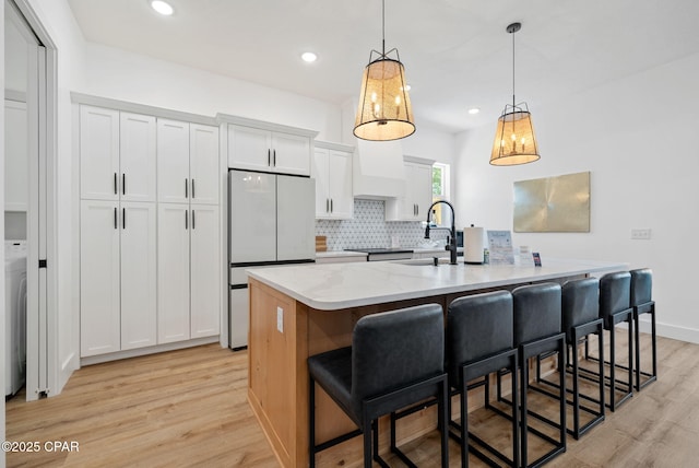 309 Tanaga St, Panama City Beach, FL 32413 - kitchen featuring freestanding refrigerator, light wood-type flooring, tasteful backsplash, a kitchen breakfast bar, and white cabinetry