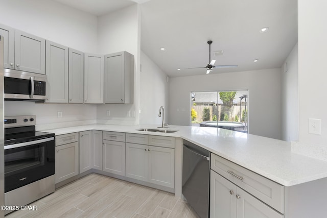 101 Loblolly Ct, Panama City Beach, FL 32413 - kitchen with stainless steel appliances, a sink, a peninsula, a ceiling fan, and gray cabinetry