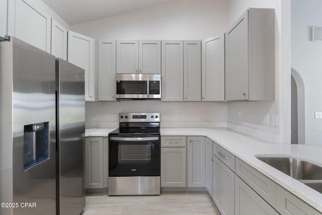 101 Loblolly Ct, Panama City Beach, FL 32413 - kitchen with stainless steel appliances, lofted ceiling, gray cabinetry, arched walkways, and light stone counters