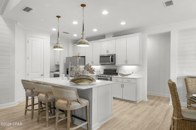 8648 Conch Shell Ct, Panama City Beach, FL 32413 - kitchen featuring appliances with stainless steel finishes, white cabinetry, a breakfast bar, an island with sink, and light wood-type flooring