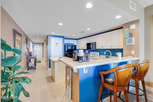 10811 Front Beach Rd Unit 2304, Panama City Beach, FL 32407 - kitchen featuring black appliances, a textured ceiling, a peninsula, a kitchen breakfast bar, and white cabinets