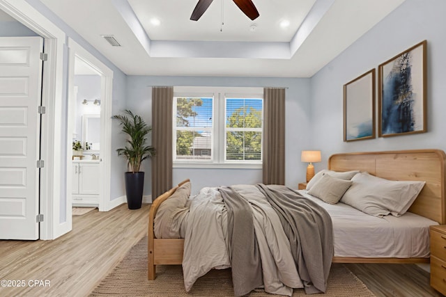 112 Christopher Dr Unit B, Panama City Beach, FL 32413 - bedroom featuring a tray ceiling, light wood finished floors, connected bathroom, and a ceiling fan
