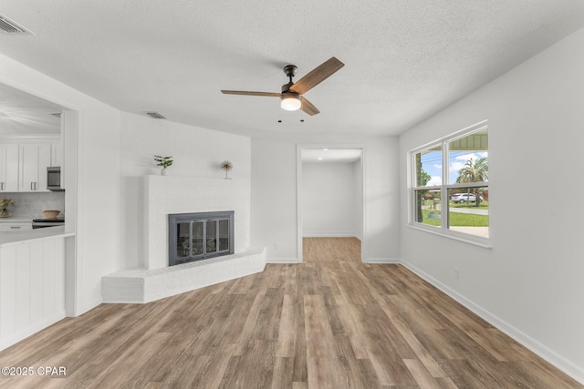 2020 Greenbriar Blvd, Lynn Haven, FL 32444 - unfurnished living room with a ceiling fan, wood finished floors, a textured ceiling, and a brick fireplace
