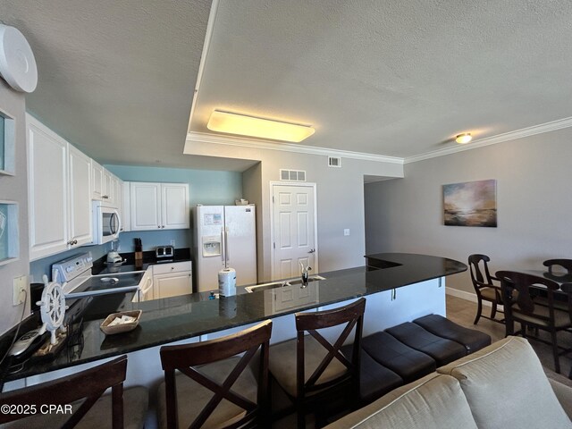 16819 Front Beach Rd Unit 107, Panama City Beach, FL 32413 - kitchen with white appliances, dark countertops, a peninsula, a breakfast bar area, and white cabinetry