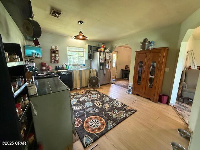 2735 E 12th St, Panama City, FL 32401 - kitchen with stainless steel fridge with ice dispenser, black dishwasher, light wood finished floors, and hanging light fixtures