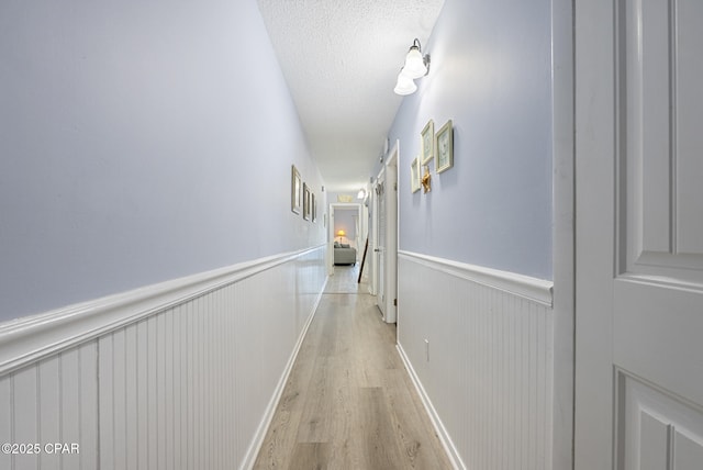 8743 Thomas Dr Unit 928, Panama City Beach, FL 32408 - hallway featuring light wood-style floors, wainscoting, and a textured ceiling