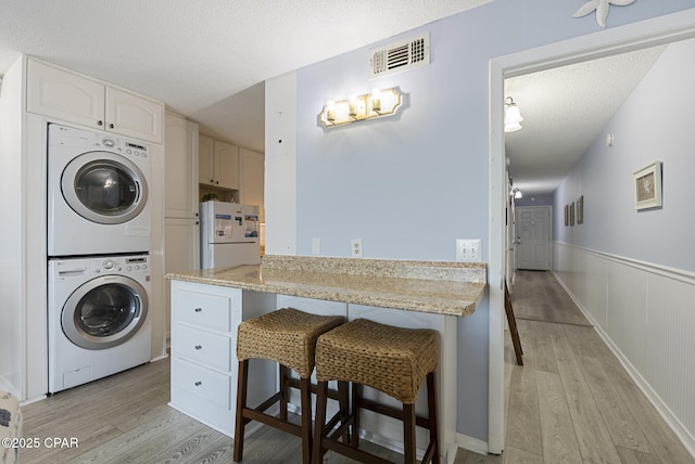 8743 Thomas Dr Unit 928, Panama City Beach, FL 32408 - washroom with estacked washer and dryer, light wood-type flooring, a wainscoted wall, and a textured ceiling