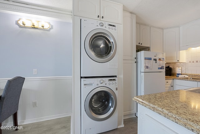 8743 Thomas Dr Unit 928, Panama City Beach, FL 32408 - laundry room featuring estacked washer and dryer, light wood-type flooring, a textured ceiling, and a wainscoted wall