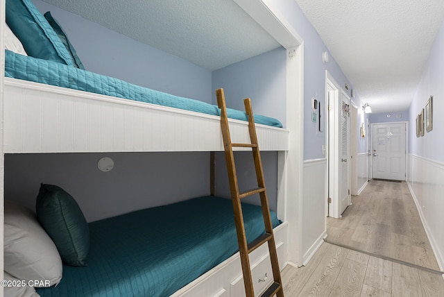8743 Thomas Dr Unit 928, Panama City Beach, FL 32408 - bedroom with wood finished floors, a textured ceiling, and a wainscoted wall