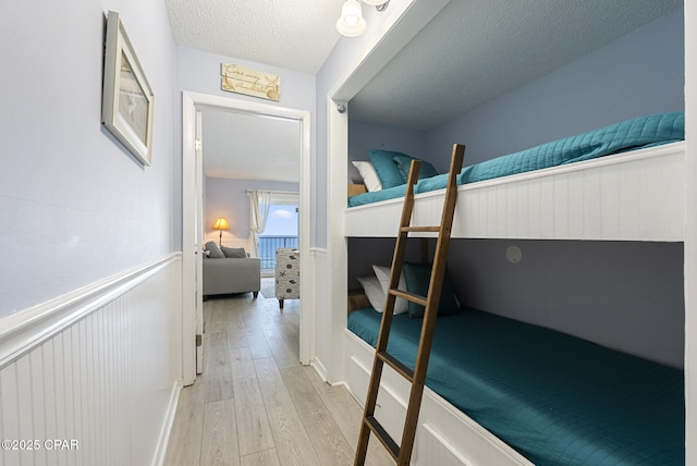 8743 Thomas Dr Unit 928, Panama City Beach, FL 32408 - bedroom with light wood-style floors, a textured ceiling, and a wainscoted wall