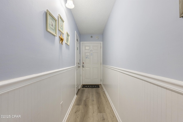 8743 Thomas Dr Unit 928, Panama City Beach, FL 32408 - hallway featuring light wood-style floors, a wainscoted wall, and a textured ceiling