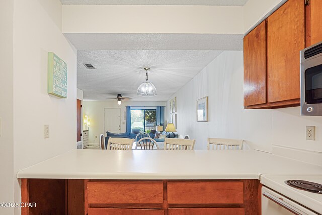 17620 Front Beach Rd Unit 4U, Panama City Beach, FL 32413 - kitchen with light countertops, stainless steel microwave, a ceiling fan, brown cabinetry, and a peninsula