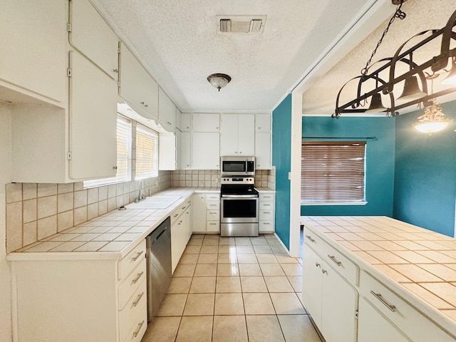 kitchen with light tile patterned floors, stainless steel appliances, tile counters, white cabinets, and decorative backsplash