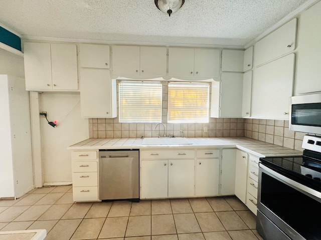 kitchen with sink, stainless steel appliances, tasteful backsplash, tile counters, and white cabinets