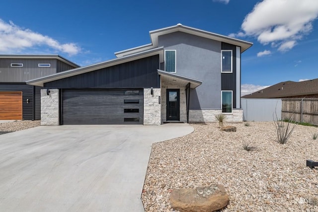 contemporary house featuring concrete driveway, a garage, fence, and stone siding