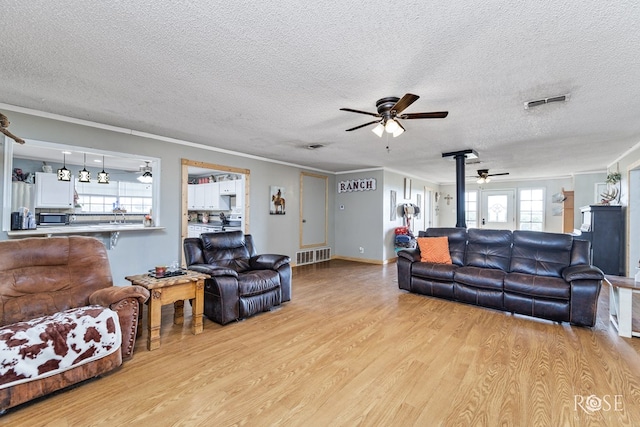 living room featuring a wood stove, ceiling fan, crown molding, a textured ceiling, and light hardwood / wood-style flooring