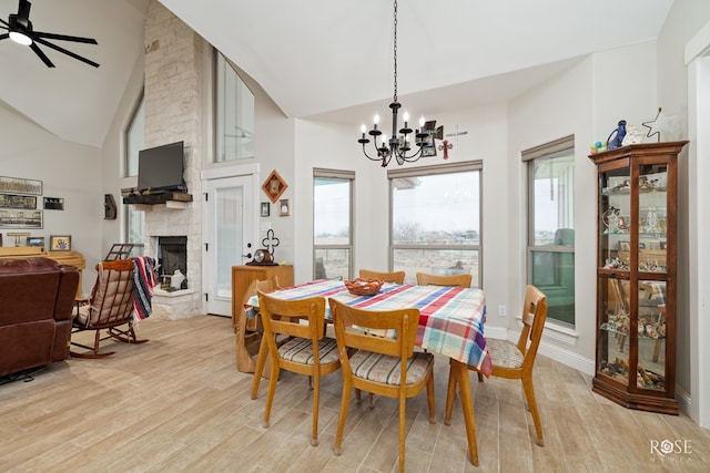 dining room with ceiling fan with notable chandelier, light hardwood / wood-style floors, a stone fireplace, and a healthy amount of sunlight