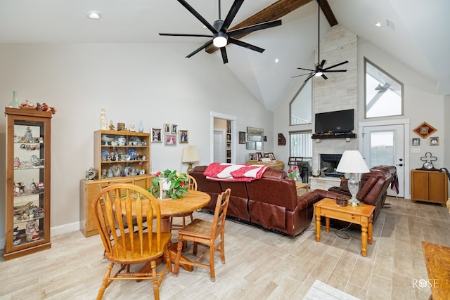 dining area featuring light hardwood / wood-style flooring, beamed ceiling, a stone fireplace, ceiling fan, and high vaulted ceiling