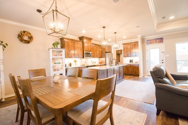 dining area with crown molding, a notable chandelier, hardwood / wood-style flooring, and sink