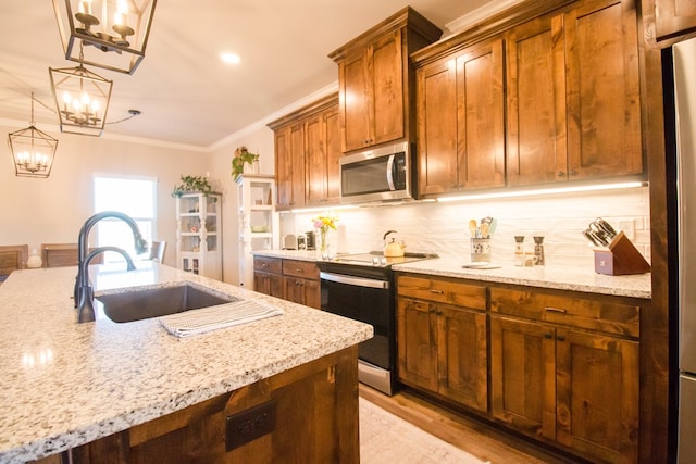 kitchen with sink, light stone counters, decorative light fixtures, ornamental molding, and appliances with stainless steel finishes