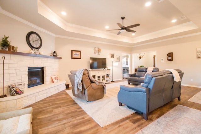 living room featuring hardwood / wood-style flooring, ornamental molding, a fireplace, and a raised ceiling