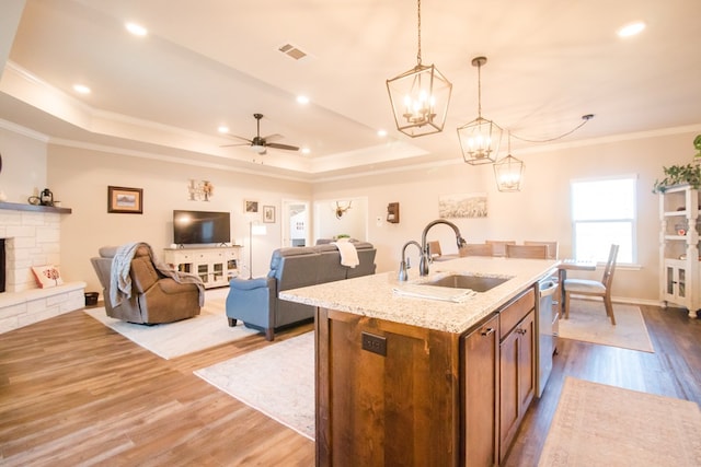 kitchen featuring sink, hanging light fixtures, light wood-type flooring, an island with sink, and a fireplace