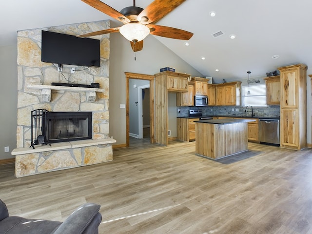 kitchen with light hardwood / wood-style flooring, hanging light fixtures, stainless steel appliances, a kitchen island, and a stone fireplace